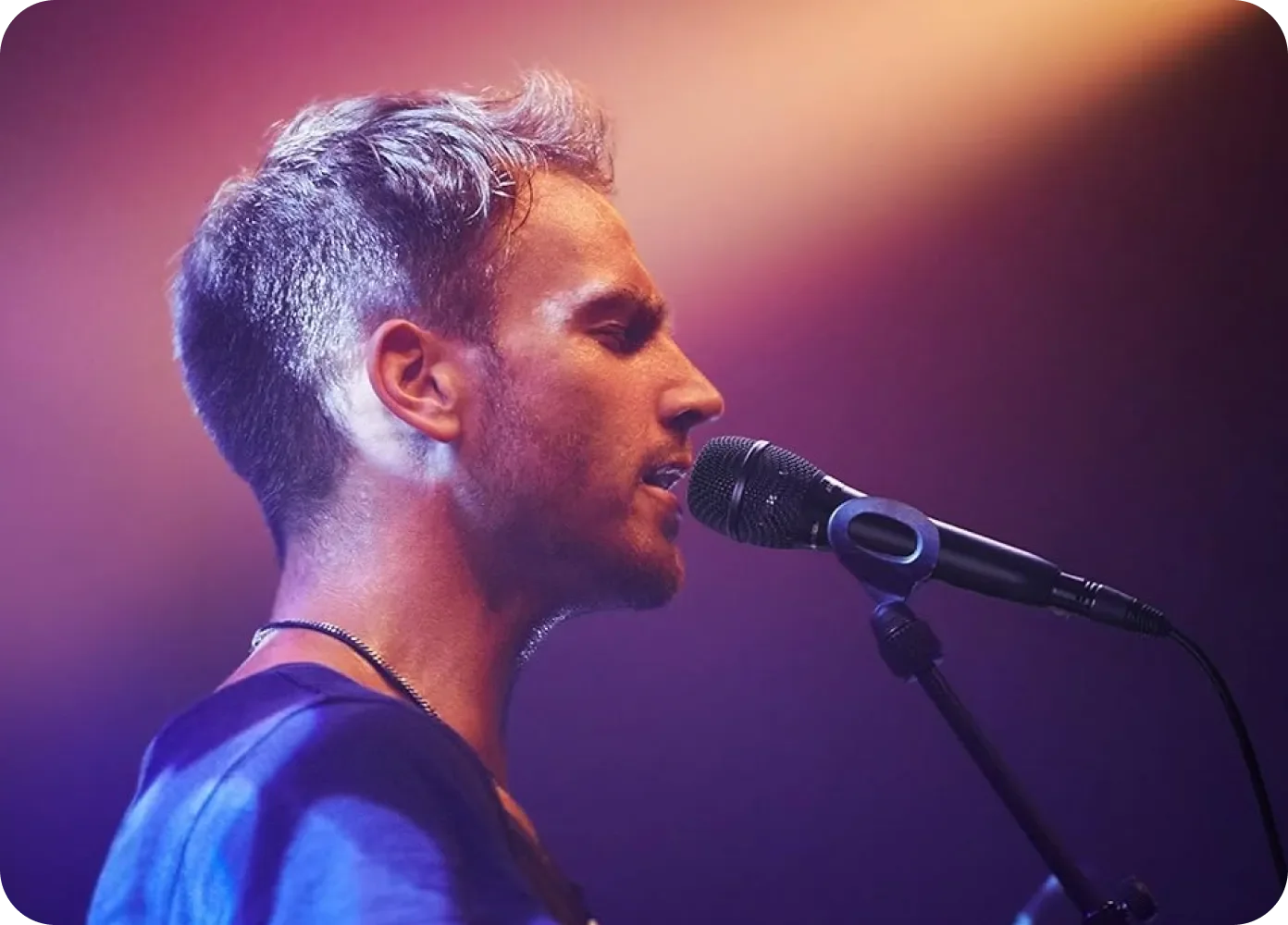 A closeup of a man singing on stage into a microphone