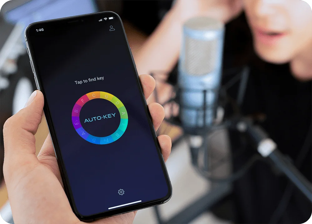 A close up shot of a hand holding an iphone with AutoKey Mobile by AutoTune on it near a person singing into a microphone