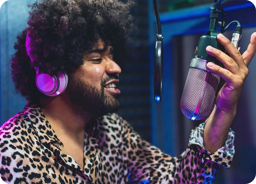 A man in the recording studio wearing headphones and grabbing on to microphone while singing