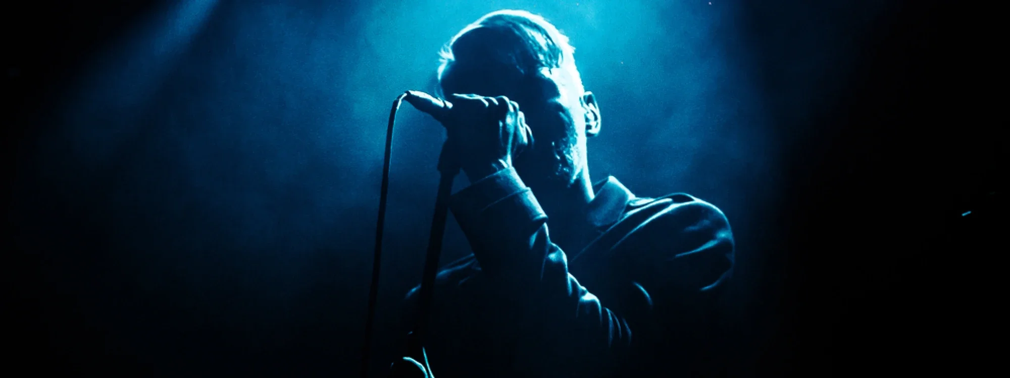 A man singing into a microphone under a haze of blue light