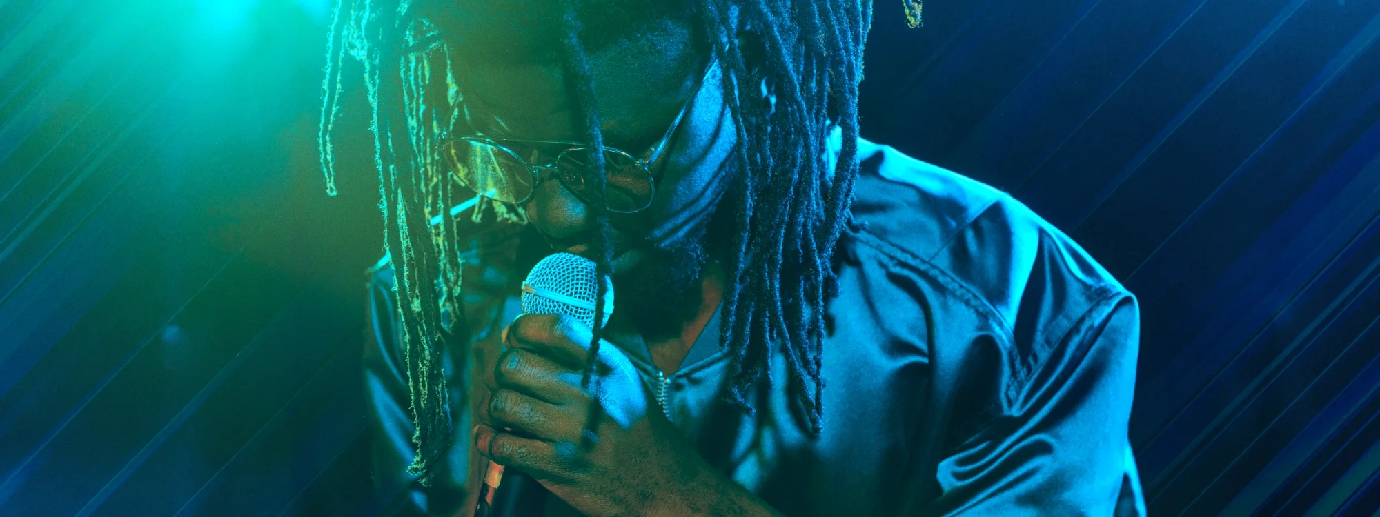 A man looking down and singing into a microphone