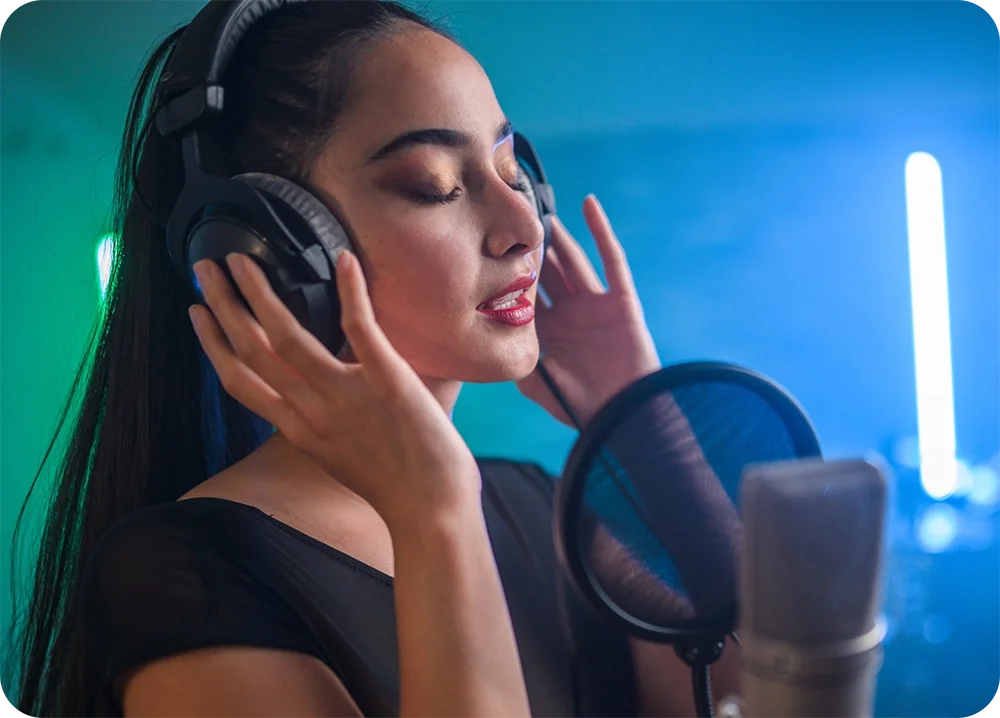 a female holding her headphones on her ears singing into a microphone in there home studio