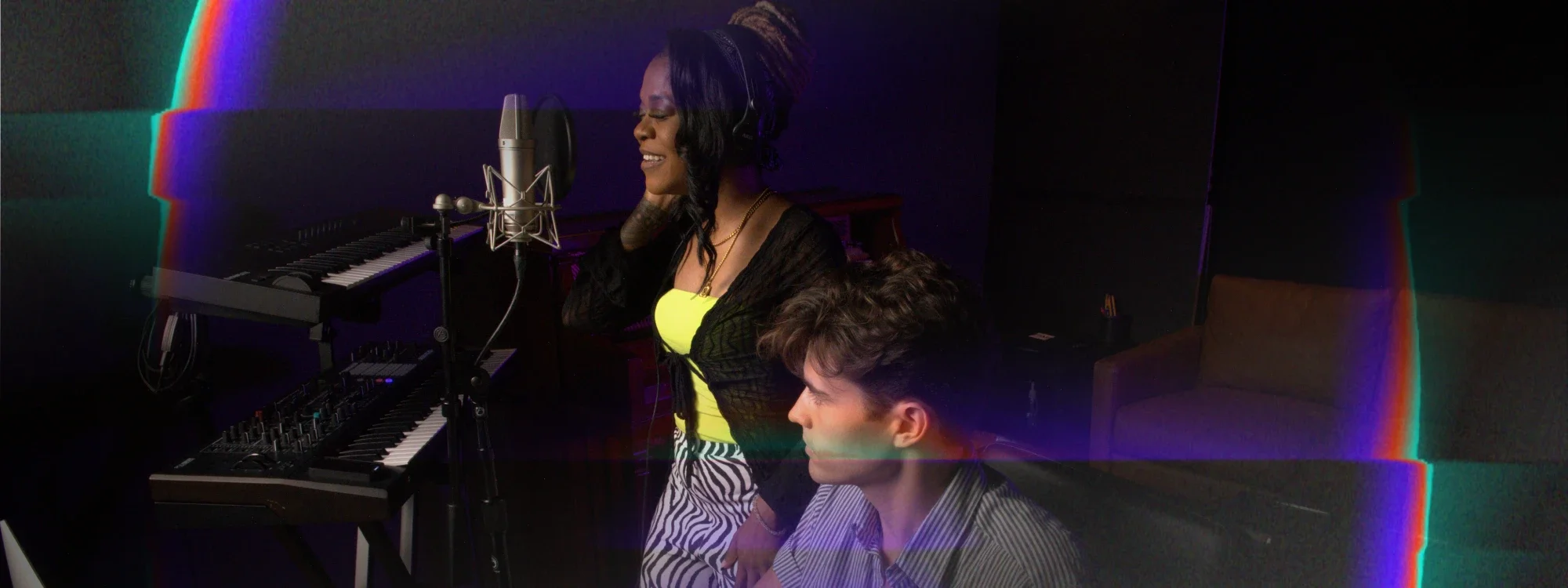 A woman standing up and singing into a microphone with a man sitting down next to her