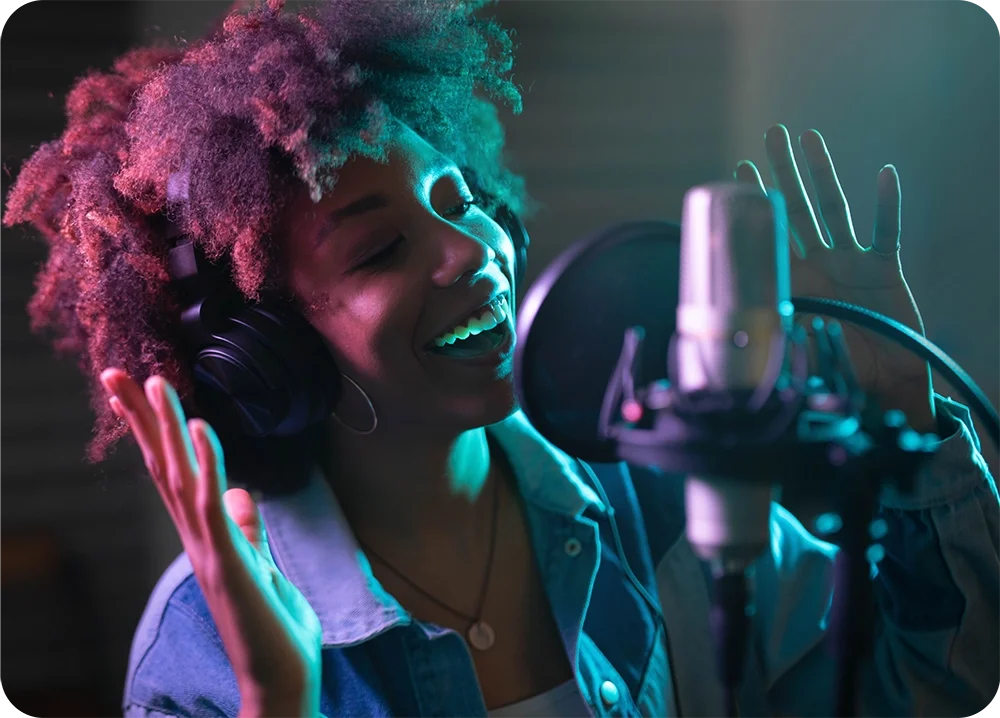 A female in the recording studio wearing headphones and singing into a microphone with pop filter