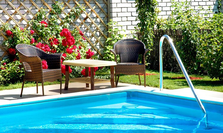 A backyard inground pool with patio chairs beside.