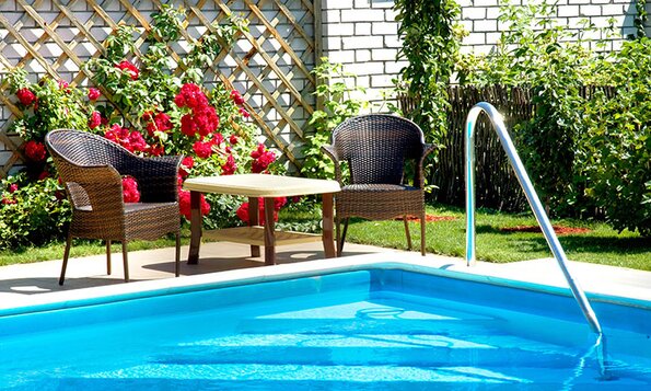A backyard inground pool with patio chairs beside.