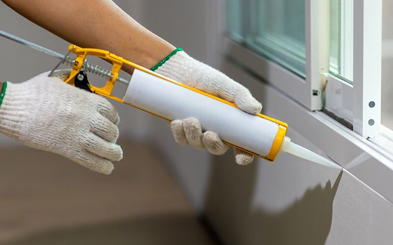 A person using a caulking gun to seal around a window. 