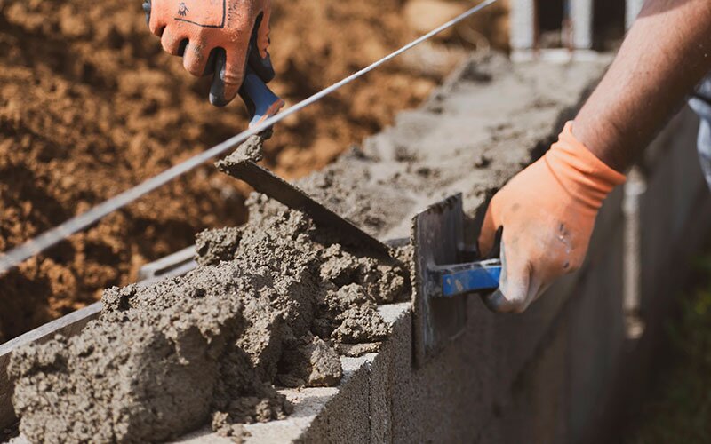 A tradesman working with concrete on a brick wall.