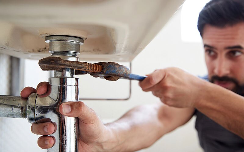 A man using a wrench to fix a leaky sink.