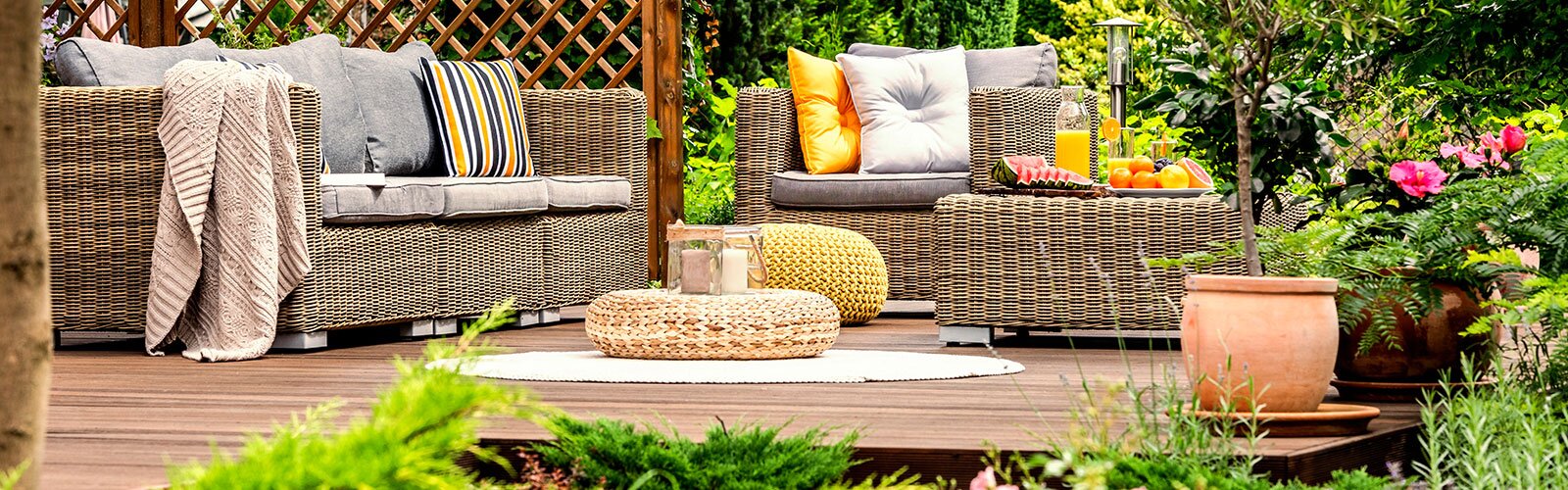 A bright and colorful outdoor patio with wicker furniture, plants, solar lights, pillows, and a fence. 