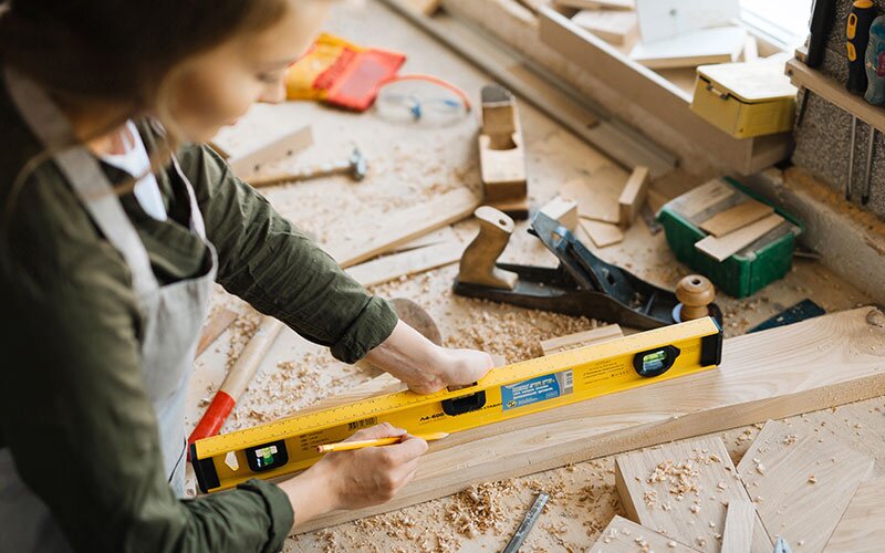 A female workshop worker uses a level on a piece of lumber.