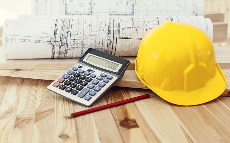 A calculator, a yellow hard hat, and blueprints sit on some lumber.