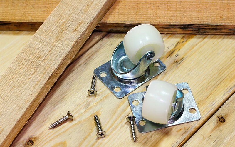 Two castors sit on lumber beside a few screws. 