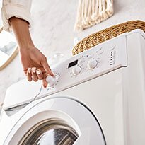 A hand touches the dial on a front load washer.