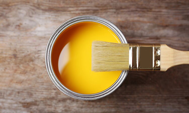 A open, yellow can of paint with a brush on top.
