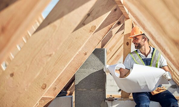 A satisfied contractor holding blueprints in a truss.