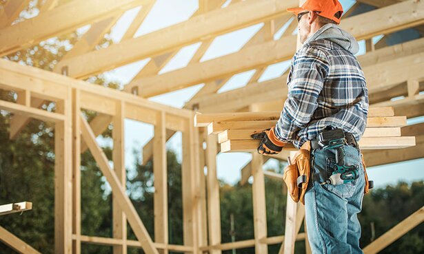 A contractor holding lumber in a building under construction.