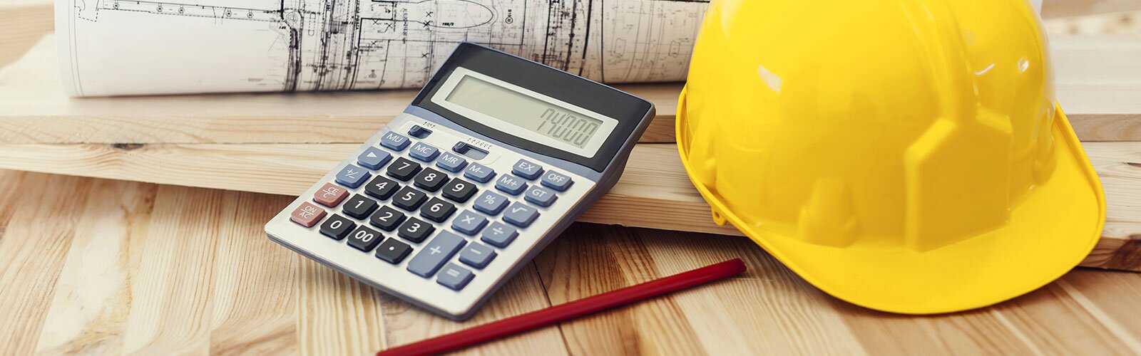 A yellow hard hat, a calculator, blueprints, and lumber displayed on a wooden surface. 