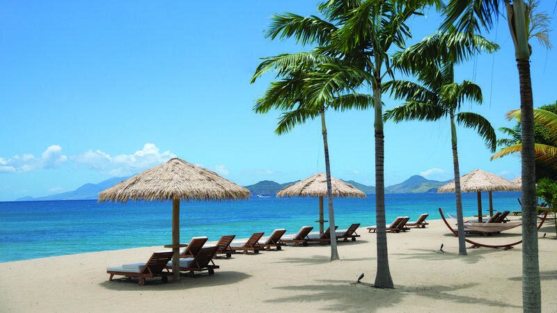 Beach chairs covered by palapas overlooking beautiful blue water.