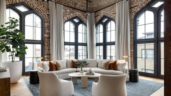 Living area with cream colored furniture arranged in a circle on a large blue area rug with all-black kitchen with stainless steel appliances with a large island