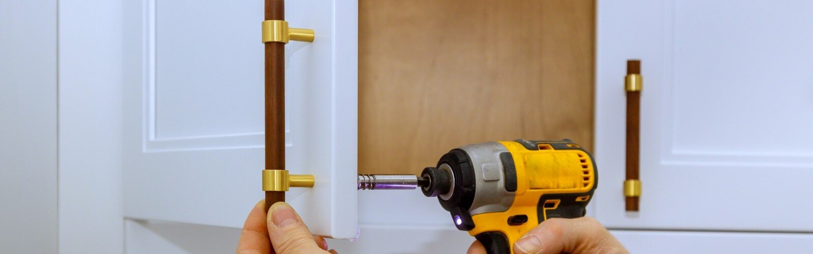 Worker uses power drill to attach cabinet handles in stylish kitchen