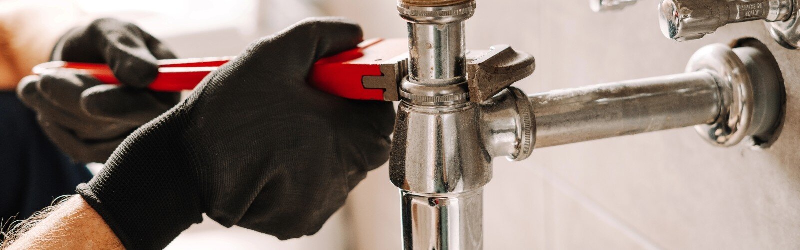 Plumber in black gloves fixes a sink pipe with a wrench in a bathroom
