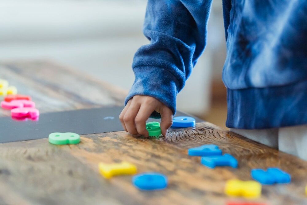 Person's hand reaching toward plastic numbers splayed across a wooden tabletop