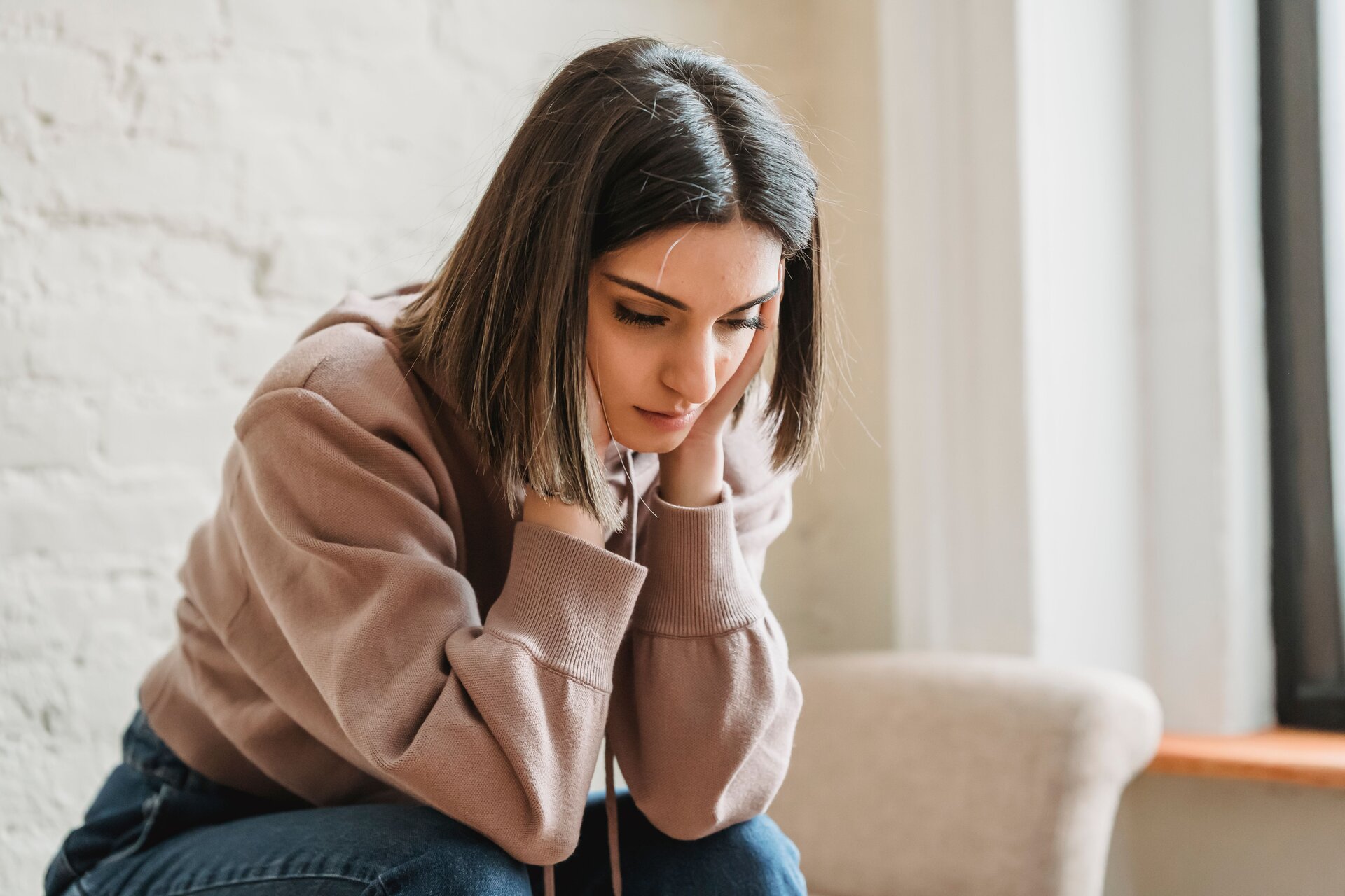 A seated young woman stares downward while holding her head in her hands