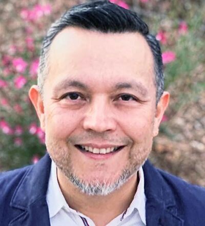 A smiling woman outdoors with a blue sky in the background.