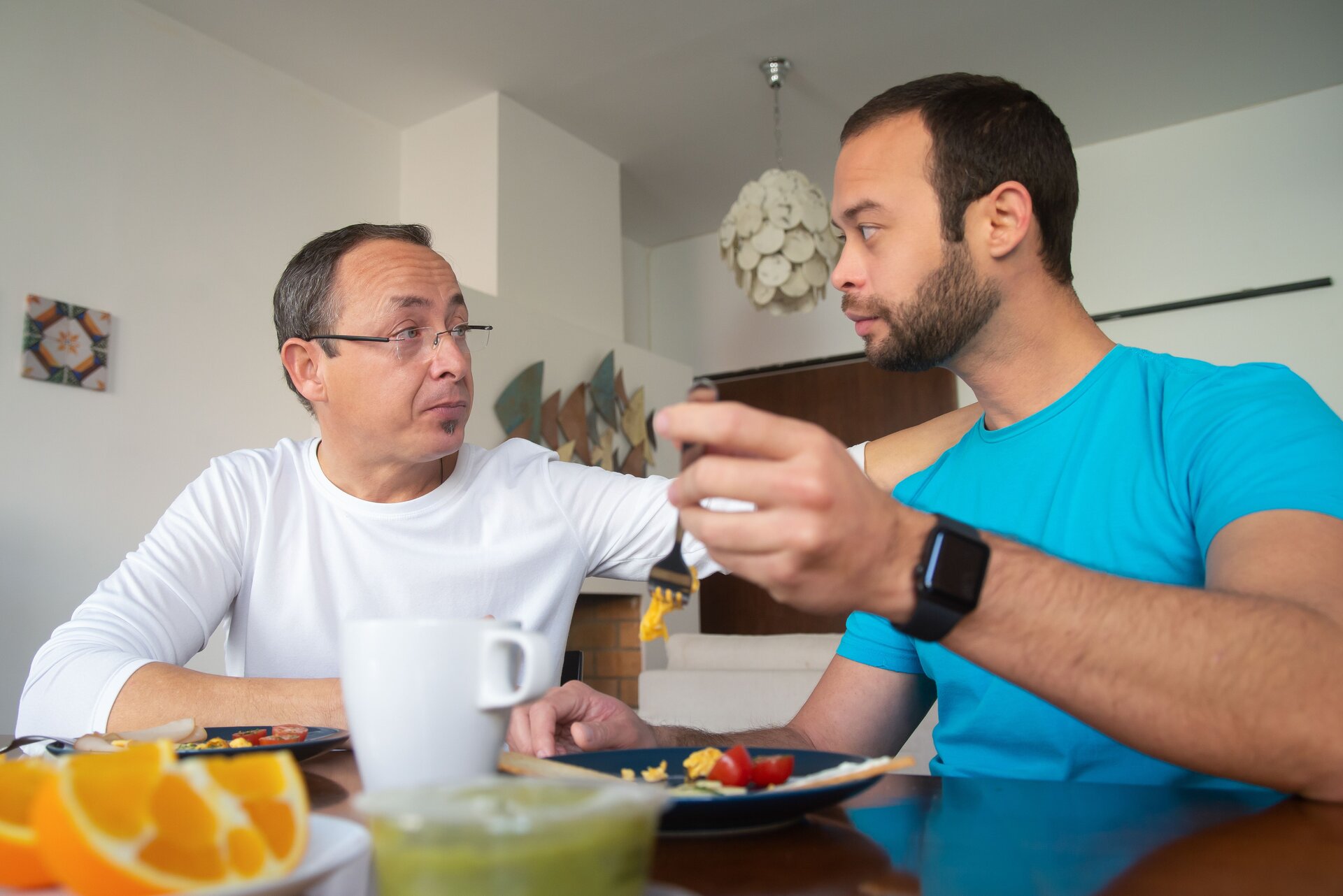 A man and his father sitting at a table looking at each other gravely