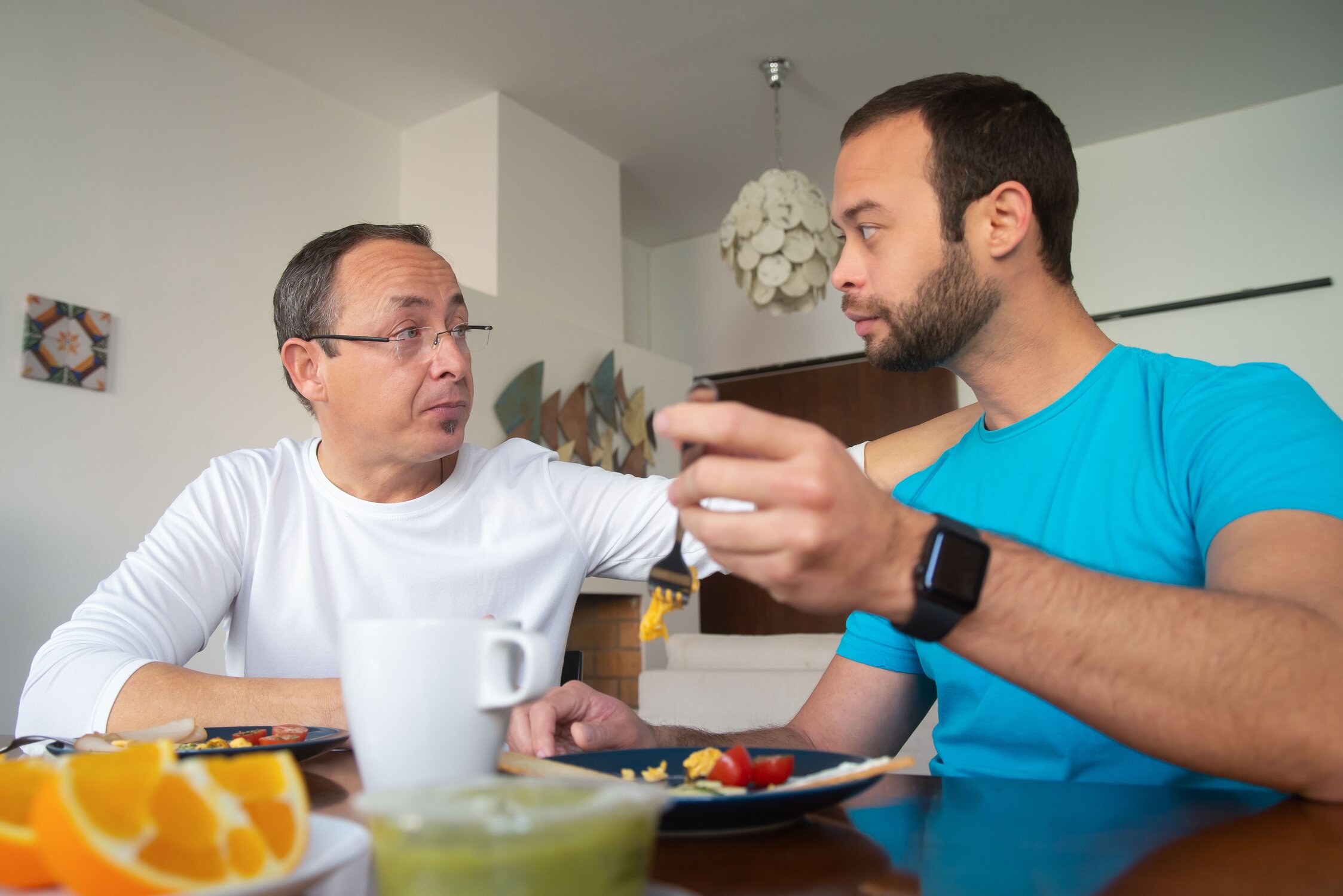 A man and his father sitting at a table looking at each other gravely
