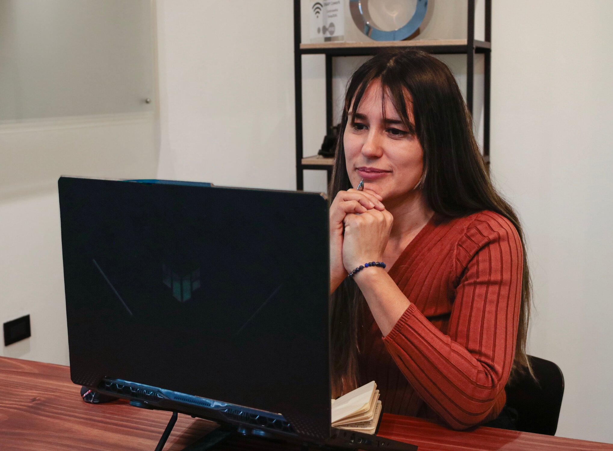 Woman in a light brown sweater sits attentively at a laptop for an online therapy call
