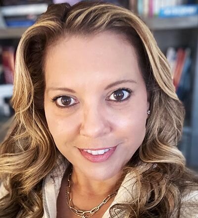 A smiling woman outdoors with a blue sky in the background.