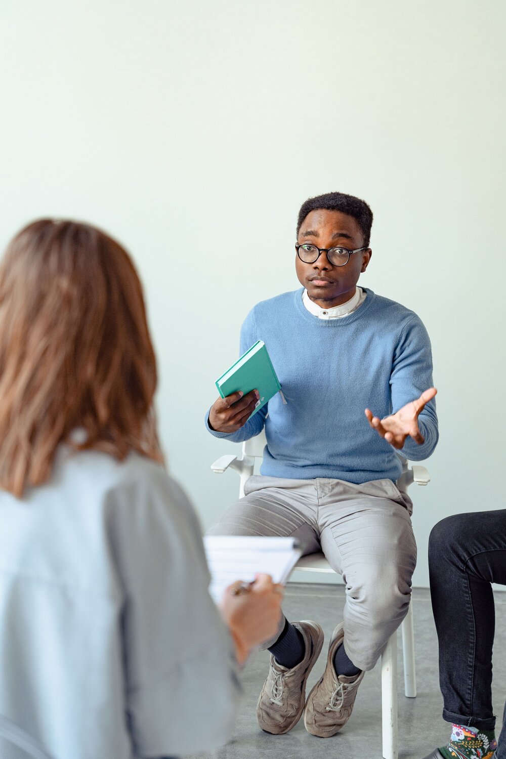 A seated man speaking with a therapist while gesturing with his hands