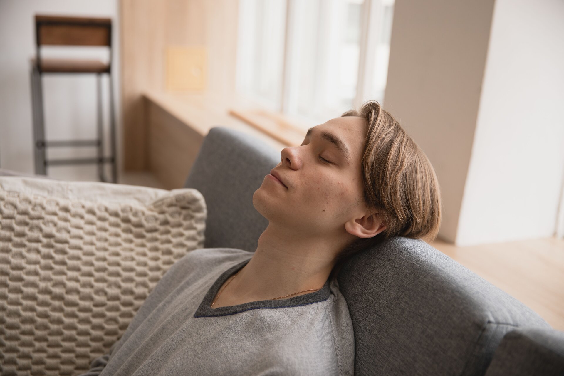 A young man sits ansd rests his head on the back of a couch with his eyes closed