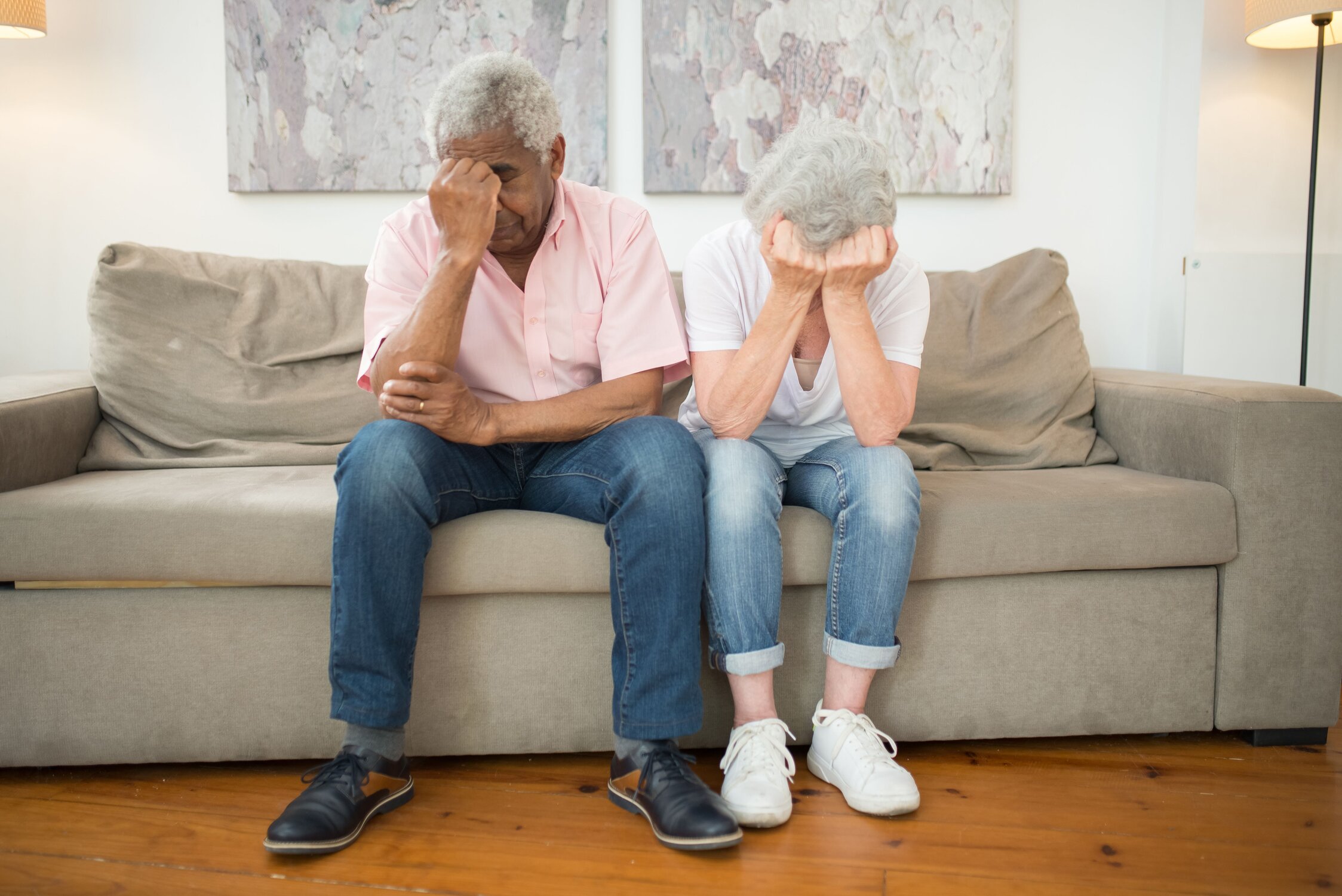 A man and woman sitting next to each other on a couch with their hands covering their faces