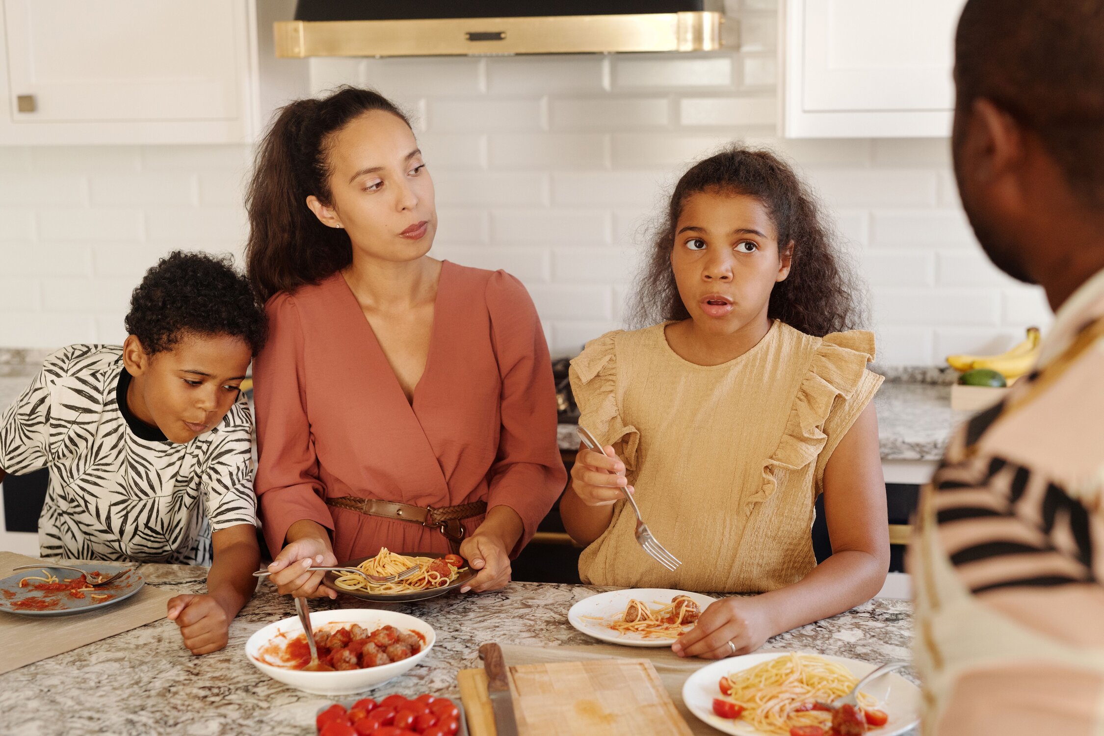 A woman standing at a kitchen counter with a young child standing on each side