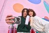 Guy and girl taking a selfie in front of a colorful wall, holding grey and tan 24oz Owala tumblers.