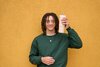 Guy in a green sweater standing in front of a bright yellow wall, holding a tan 24oz Owala tumbler.