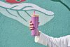 Person in a white sweater holding a pink 24oz Owala tumbler in front of a blue wall.