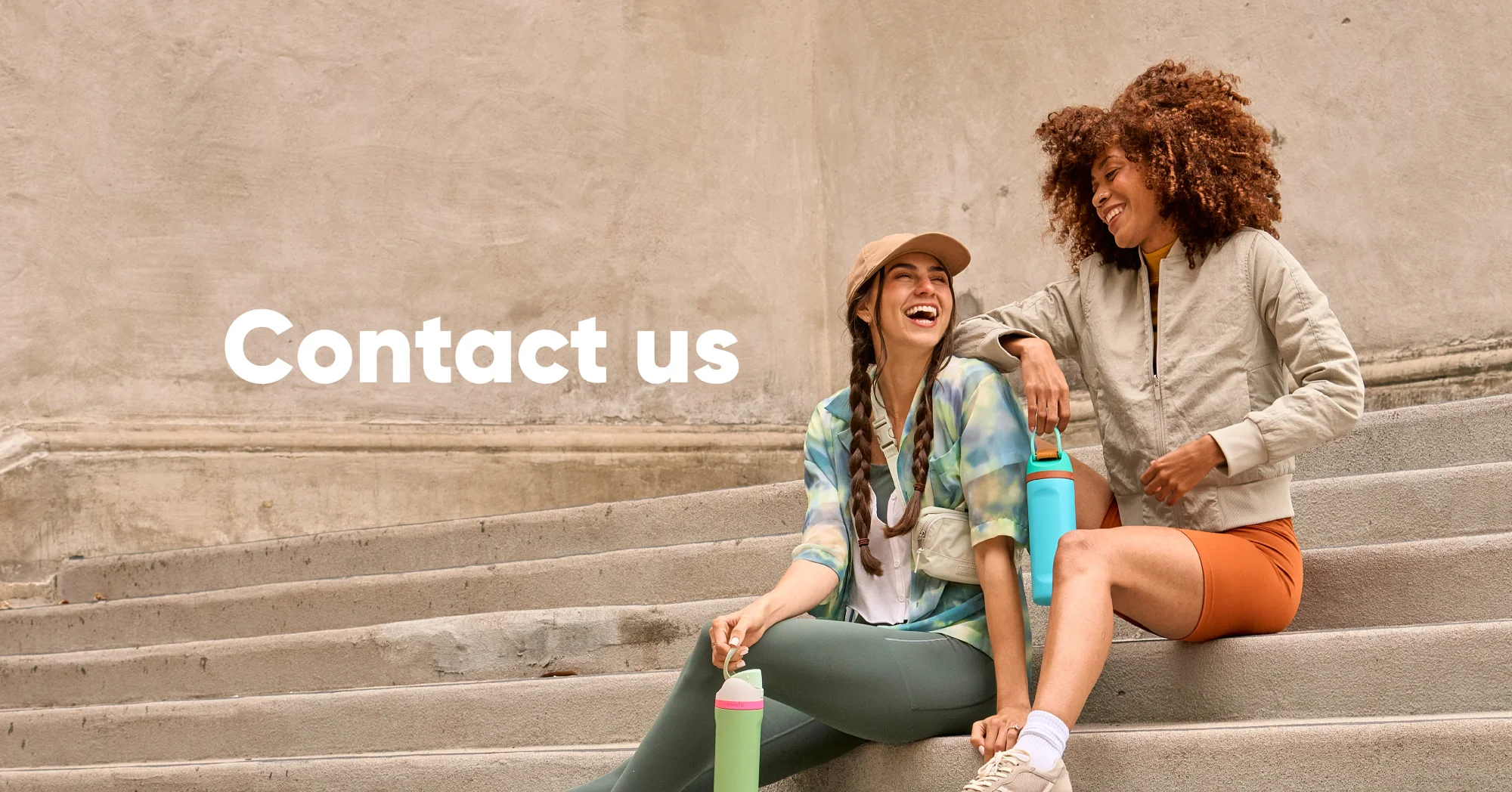 Two women sitting on stairs, holding Owala FreeSip water bottles and sharing a moment together.