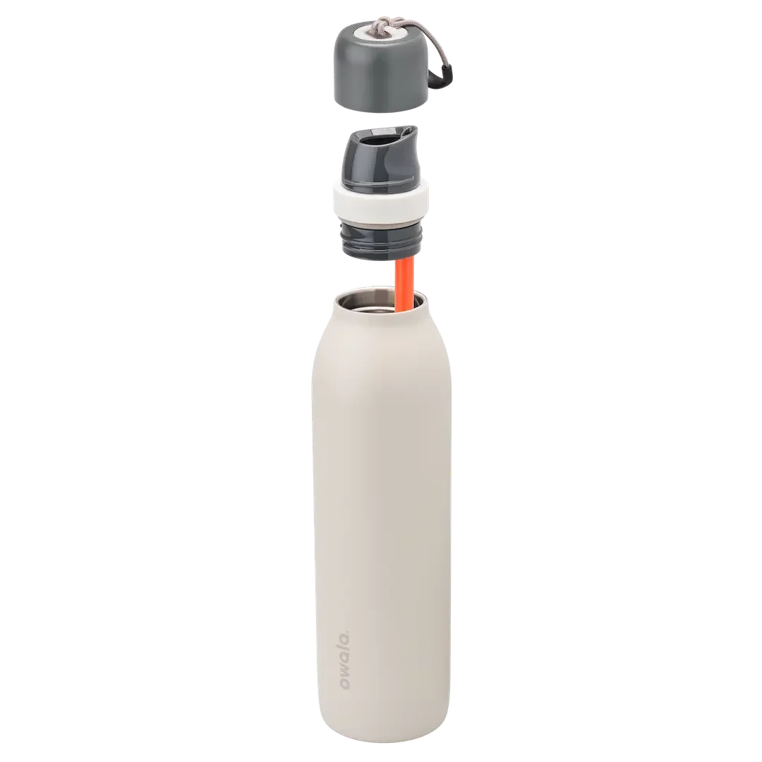 Owala FreeSip Twist 24oz in Rock On, warm off-white insulated stainless steel body with dark gray twist cap, white twist cap accent band, and tan carry string; exploded view showing dark gray FreeSip spout, orange straw, and Owala logo on body