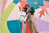 Guy and girl standing in front of a colorful abstract wall, holding tan and pink 24oz Owala tumblers.