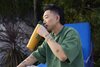 A man drinking from an orange and green FreeSip Tumbler