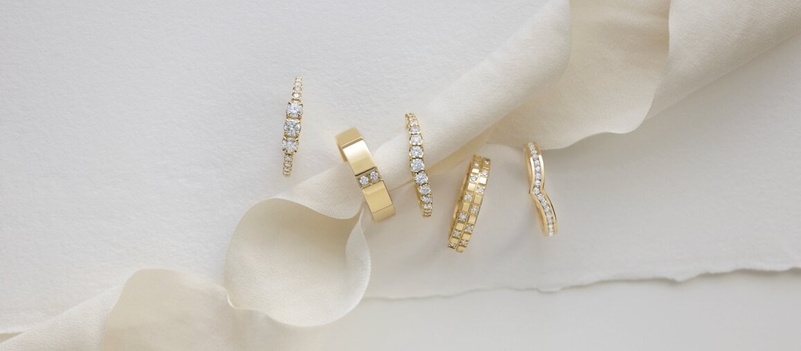 Collection of yellow gold wedding bands with pavé and channel-set diamonds displayed on soft ivory fabric