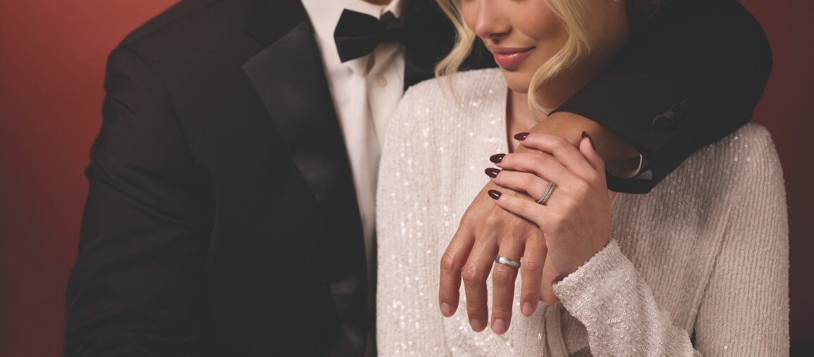 Bride and groom embracing while wearing classic wedding bands, highlighting a diamond engagement ring and a polished men’s wedding band.