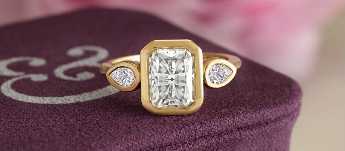 Emerald cut diamond engagement ring in a yellow gold bezel setting with marquise side diamonds by Wedding Bands & Co.