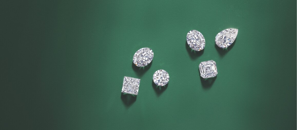 Assorted lab-grown diamonds in round, oval, pear, princess, and square cuts displayed on a green background