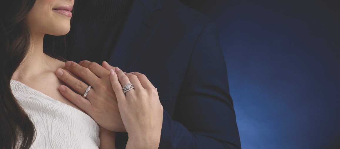 Bride and groom embracing with hands shown wearing diamond engagement ring and wedding band set symbolizing love and commitment