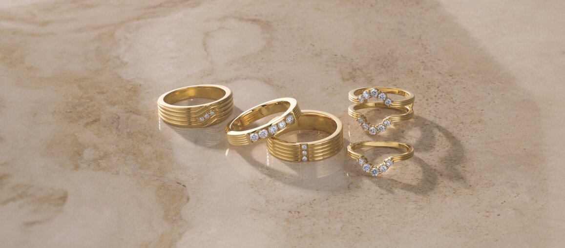Yellow gold wedding bands and diamond-accent rings displayed on stone surface featuring textured and curved designs